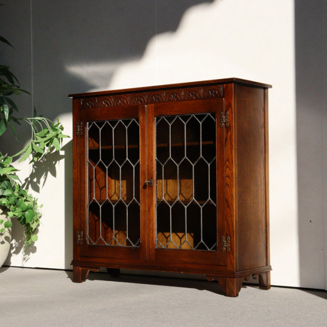 Vintage British mid-century teak cabinet by Jaycee with patterned glass doors, carved top trim, and sturdy short legs.