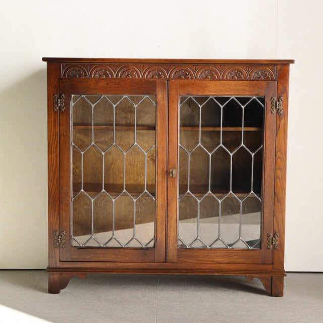 Vintage mid-century British teak cabinet by Jaycee with leaded glass doors and carved decorative trim.