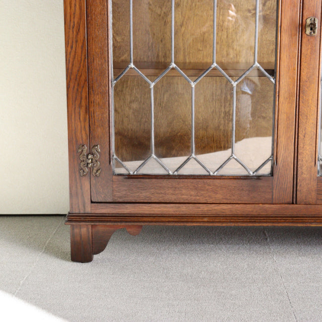 Vintage British mid-century teak cabinet corner with leaded glass door, detailed wood grain, and brass hardware from Jaycee.