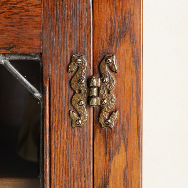 Close-up of vintage teak cabinet door hinge with intricate British mid-century design, featuring detailed brass seahorse.