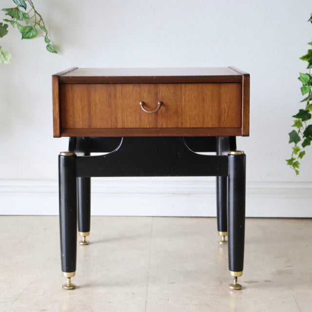 Vintage British mid-century teak bedside cabinet with black rounded legs and brass feet, single drawer with brass handle.