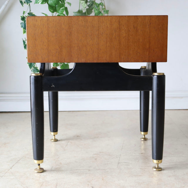 Vintage British mid-century teak bedside cabinet with black tapered legs and brass feet, sleek Danish-inspired design.