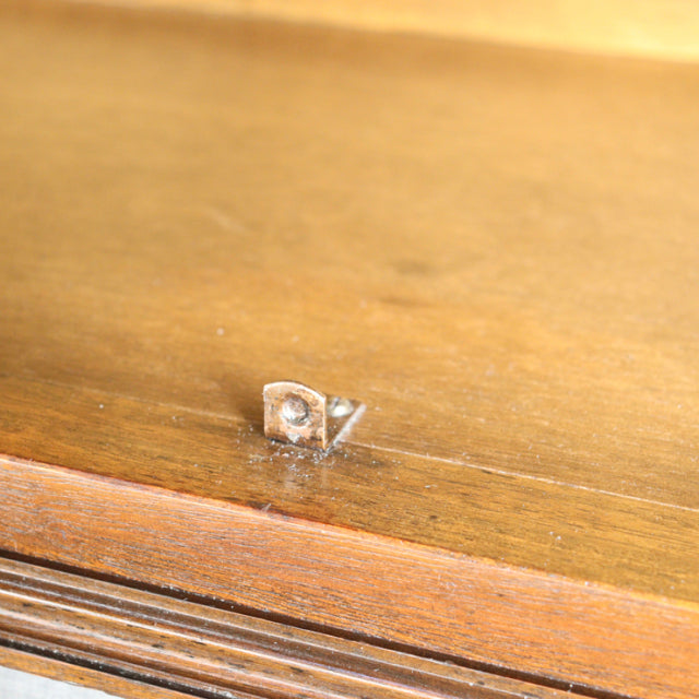 Close-up of mid-century teak wood surface with natural grain and small carved Jaycee brand mark on vintage British cabinet.