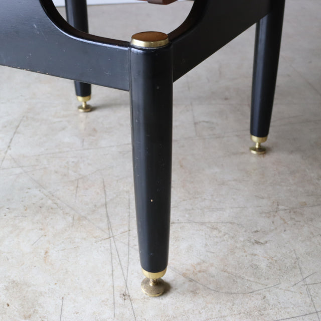 Black mid-century chair leg with brass cap and caster, showcasing vintage British teak craftsmanship.