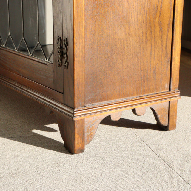 Mid-century British teak cabinet corner with rich wood grain, beveled glass door, and carved bracket feet.
