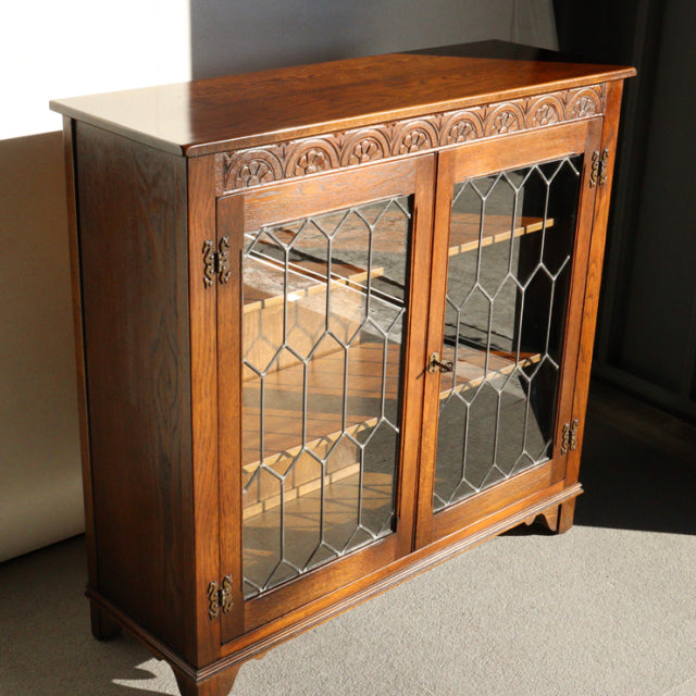 Vintage mid-century Jaycee teak cabinet with decorative carved trim, leaded glass doors, and tapered legs, British-Danish.