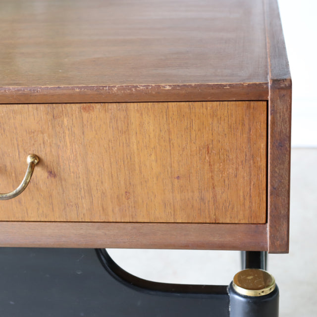 Vintage British mid-century teak bedside cabinet with brass handle, black and gold leg detail, and visible wood grain.