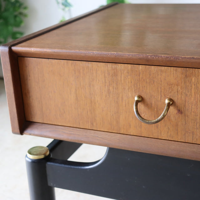 Vintage British teak bedside cabinet drawer with brass handle, black mid-century legs with brass caps, smooth wood grain.