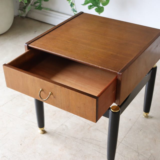 Vintage British mid-century teak bedside cabinet by G-PLAN with black tapered legs, gold ring accents, and open drawer.