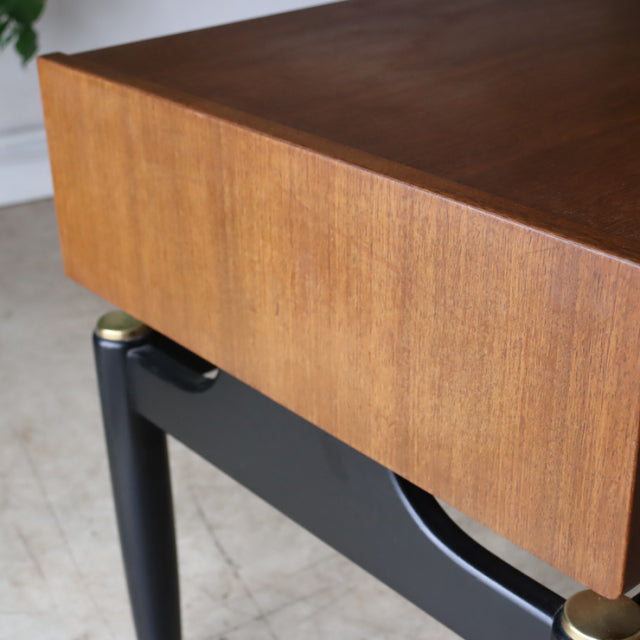 Vintage British mid-century G-Plan bedside cabinet with teak wood grain top and black legs featuring brass accents.