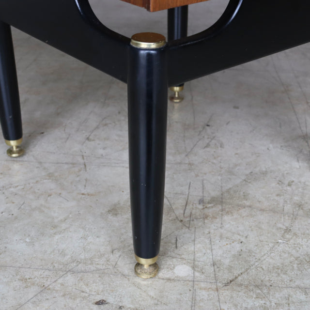 Mid-century British G-Plan bedside cabinet leg in black with brass feet, teak wood grain visible.