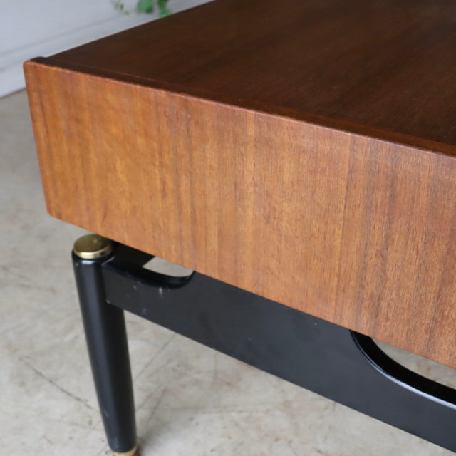 Vintage British G-Plan teak bedside cabinet with rich wood grain, black legs, and gold accents, mid-century modern design.