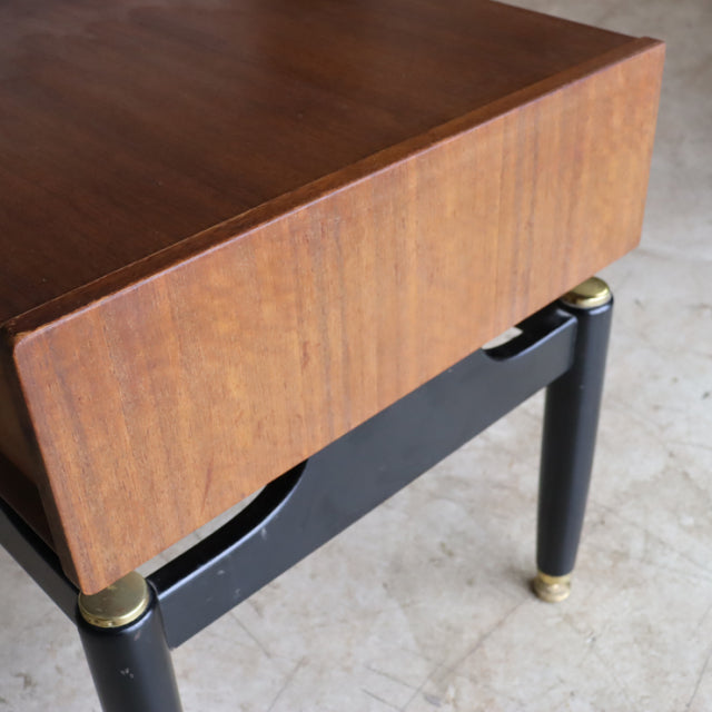 Mid-century British G-Plan bedside cabinet in teak with black legs and gold accents, showcasing rich wood grain and sleek.