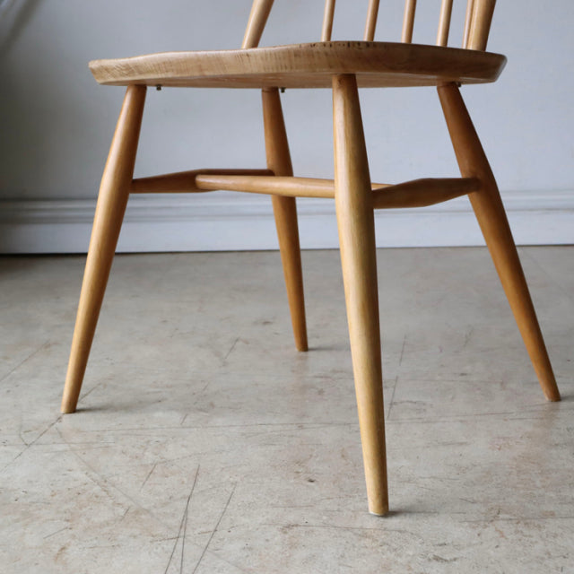 Mid-century British ERCOL Quaker chair in natural teak with smooth wood grain, tapered legs, and spindle back design.
