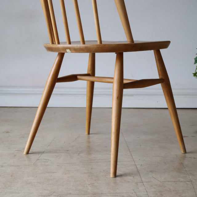 Vintage British Ercol Quaker chair in natural teak with tapered legs and spindle back, mid-century Denmark style visible.