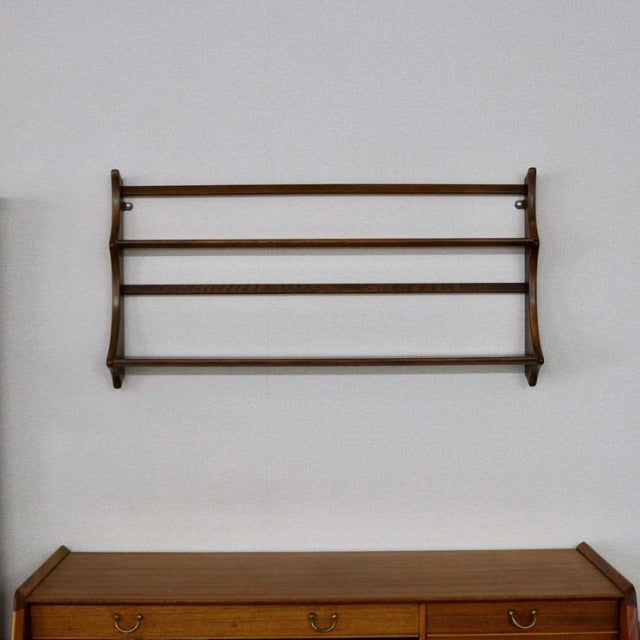 Vintage British mid-century teak Ercol plate rack with visible wood grain and rounded edges mounted on white wall above.