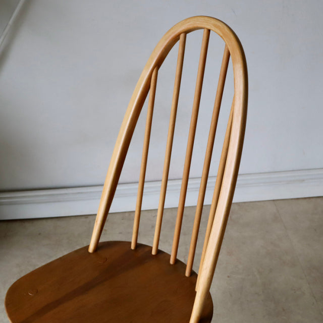 Mid-century British Ercol Quaker chair in natural teak with high, rounded spindle back and smooth wood grain on seat and legs.