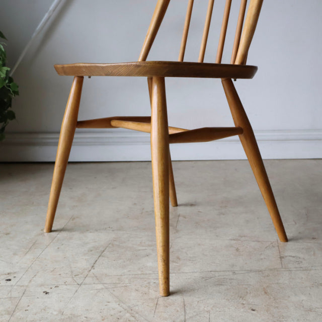 Mid-century British ERCOL Quaker chair in natural teak with sleek spindle back and tapered legs, showcasing smooth wood.