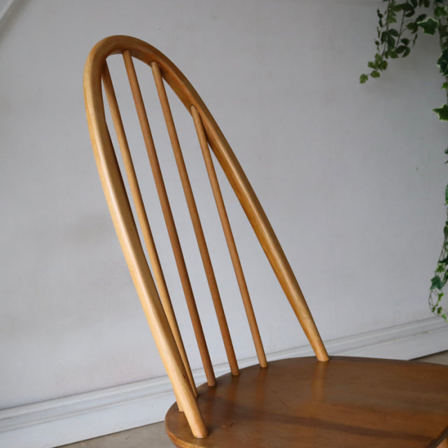 Vintage mid-century British Ercol Quaker chair in natural teak with tall curved spindle back and smooth wood grain seat.