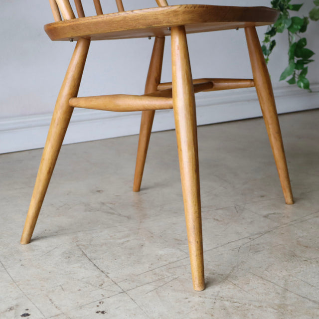Vintage British Ercol Quaker chair in natural teak with slender tapered legs and visible wood grain, mid-century Denmark.