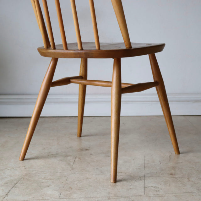 Vintage mid-century British Ercol Quaker chair in natural teak with spindle back and tapered legs showing smooth wood grain.