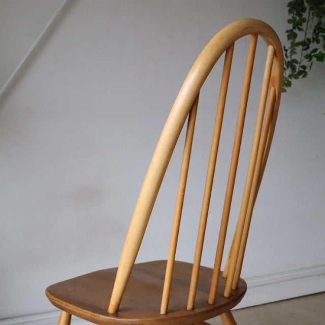 Vintage British Ercol Quaker chair in natural teak with mid-century curved spindle back and smooth wood grain seat.