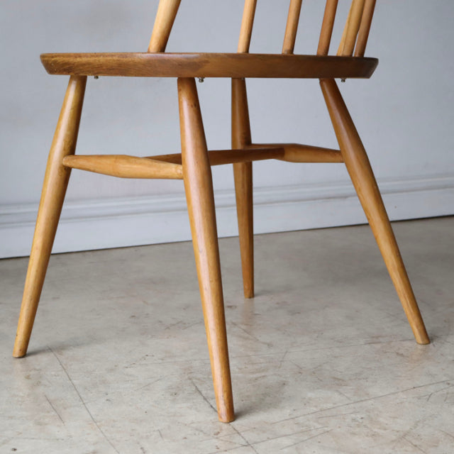 Mid-century British Ercol Quaker chair in natural teak, showcasing smooth wood grain, tapered legs, and spindle backrest.