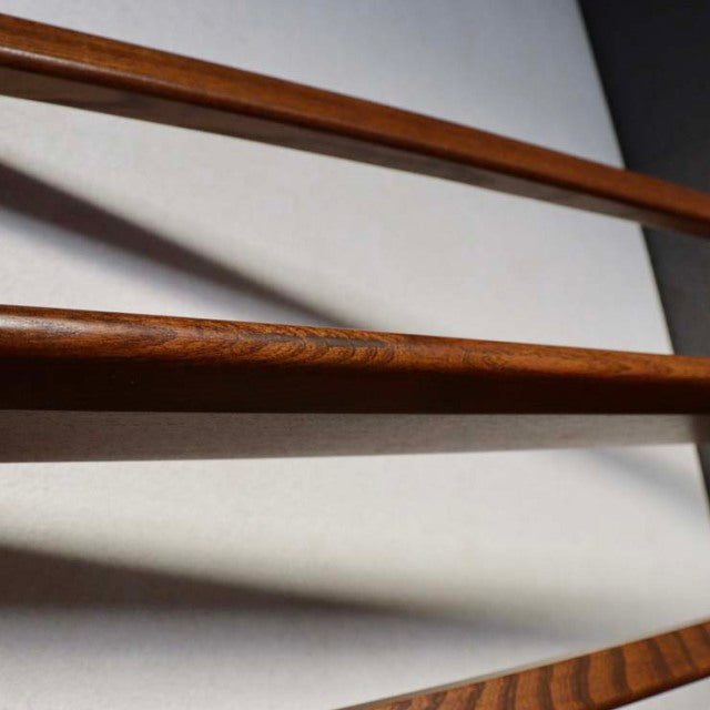 Mid-century British Ercol teak wall-mounted plate rack with rich wood grain and slender horizontal rails.