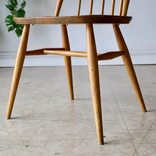 Vintage British mid-century Ercol Quaker chair in natural teak, showcasing slender spindle legs and smooth wood grain.