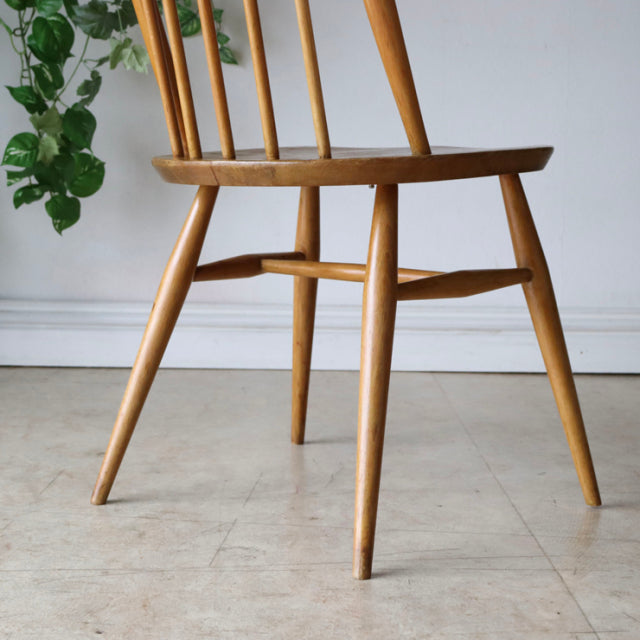 Mid-century British Ercol Quaker dining chair in natural teak with slender spindle back and tapered legs showing wood grain.