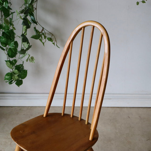 Vintage British mid-century Ercol Quaker chair in natural teak with curved spindle back and smooth wooden seat.