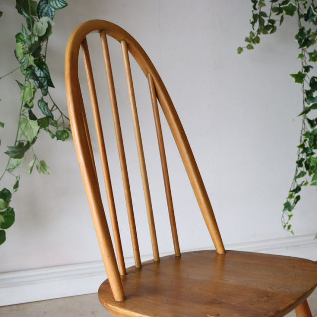 Vintage British mid-century ERCOL Quaker chair in natural teak with curved spindle back and smooth wooden seat.