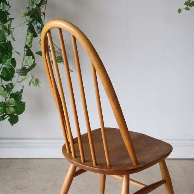 Vintage mid-century British Ercol Quaker dining chair in natural teak with curved spindle back and smooth wooden seat.