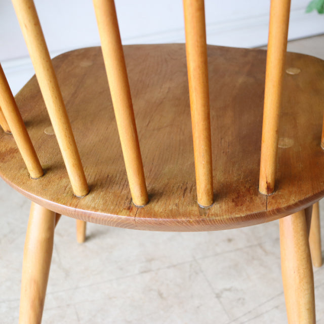 Vintage British mid-century Ercol Quaker chair in natural teak with spindle back and visible wood grain on seat and legs.
