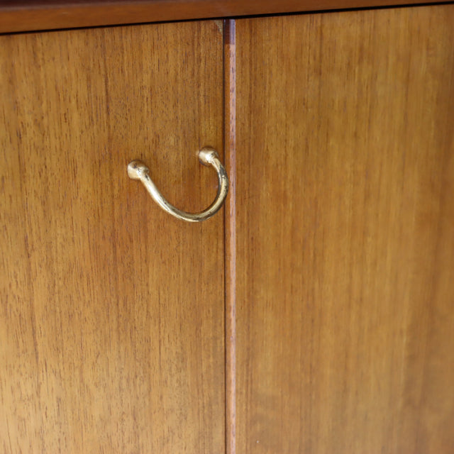 Close-up of vintage teak sideboard door with brass U-shaped handle, showcasing British mid-century wood grain and.