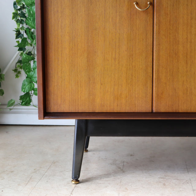 Mid-century British G-Plan teak sideboard with rich wood grain, slender black legs, and brass feet accents.