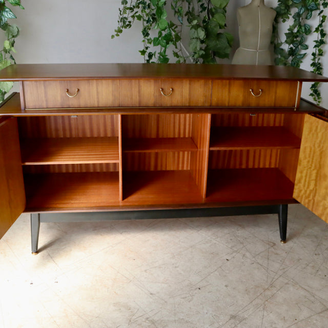 Mid-century British G-Plan teak sideboard with rich wood grain, black tapered legs, and open storage compartments.