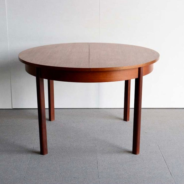 Round vintage teak dining table with mid-century British-Denmark design, smooth wood grain, slender tapered legs.