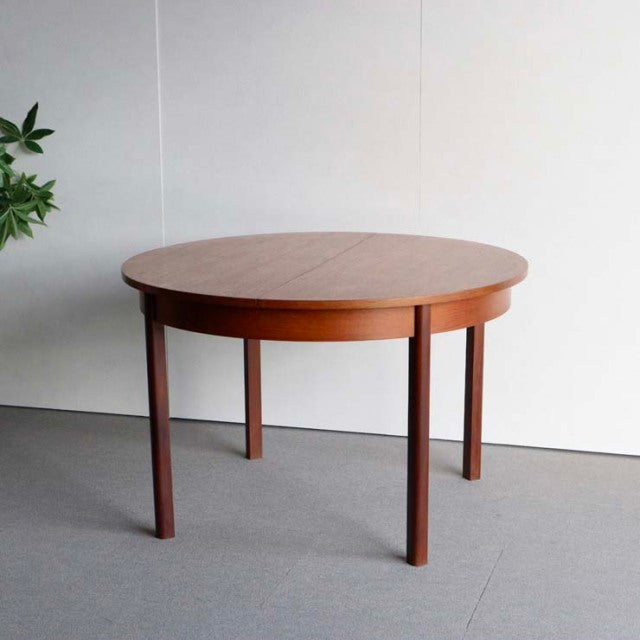 Vintage mid-century British teak dining table with round top, smooth wood grain, and slender tapered legs.