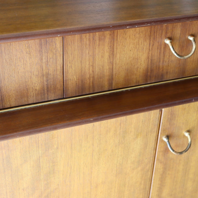 Vintage British G-Plan teak sideboard with mid-century design, rich wood grain, brass handles, and slim tapered legs.