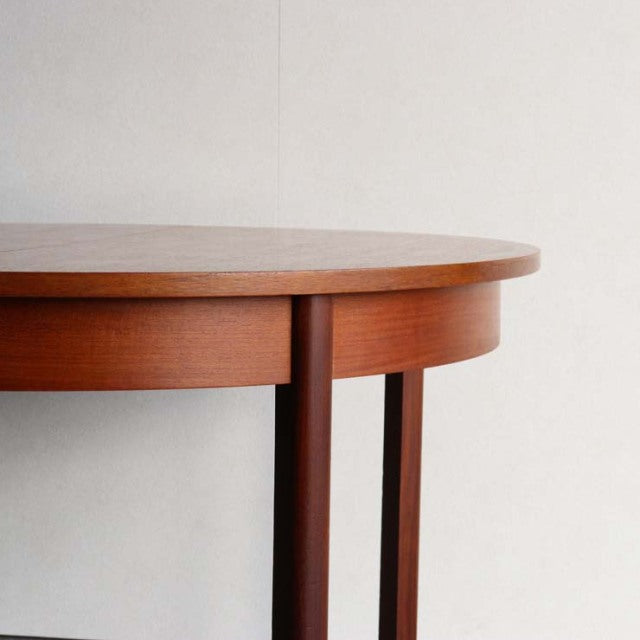 Vintage teak dining table with smooth rounded edge, slender mid-century British-style legs, showcasing rich wood grain and.