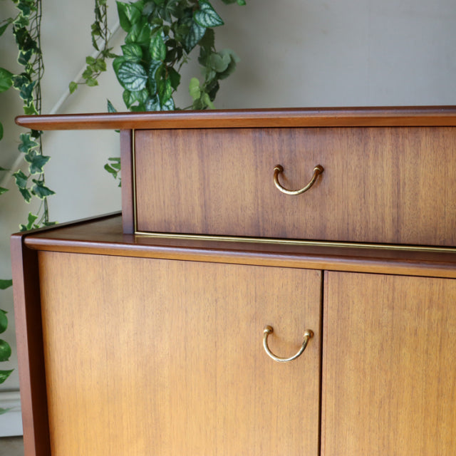 Vintage British G-Plan teak sideboard with brass handles, mid-century sleek rectangular design, rich wood grain, and raised.