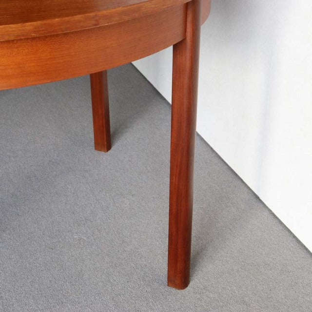 Mid-century British vintage teak dining table corner with smooth wood grain and round tapered legs against a gray floor and.