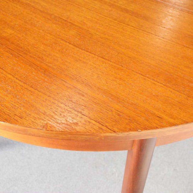 Round mid-century vintage teak dining table top with smooth wood grain and slender British-style legs.