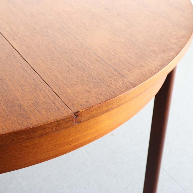 Mid-century British vintage teak dining table corner with smooth wood grain and rounded edge on slender round legs.