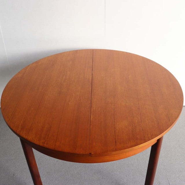 Round vintage teak dining table with smooth wood grain, slender mid-century British-style tapered legs, and an extending.