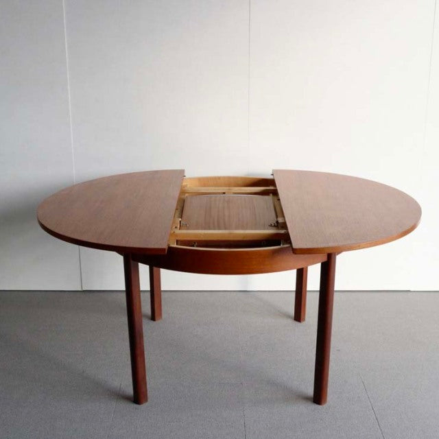 Vintage teak dining table with round mid-century British design, featuring smooth wood grain and slender tapered legs,.