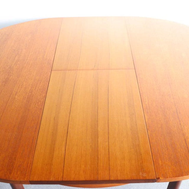 Mid-century British vintage teak dining table with smooth grain and rounded edges, extension leaf visible in center.