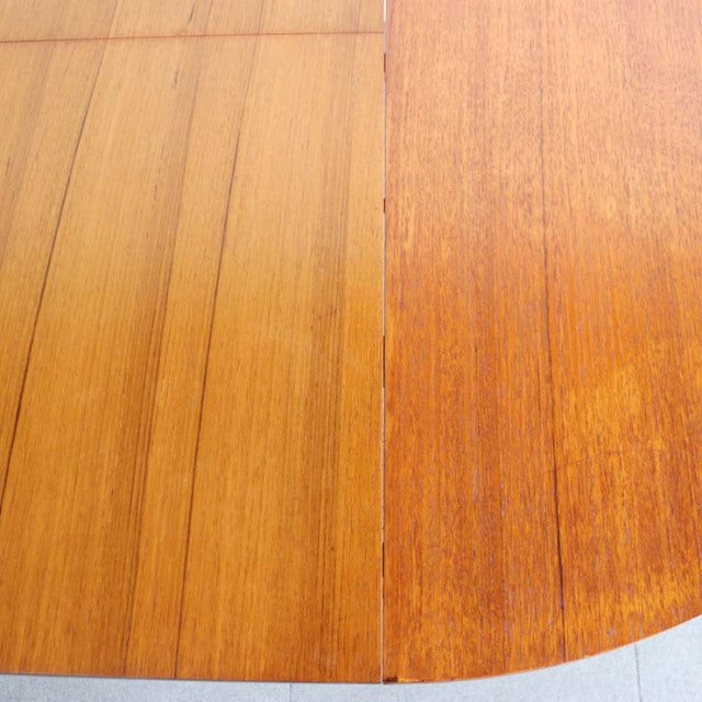 Mid-century vintage British teak dining table with rich wood grain and smooth rounded edge, extension leaf visible.