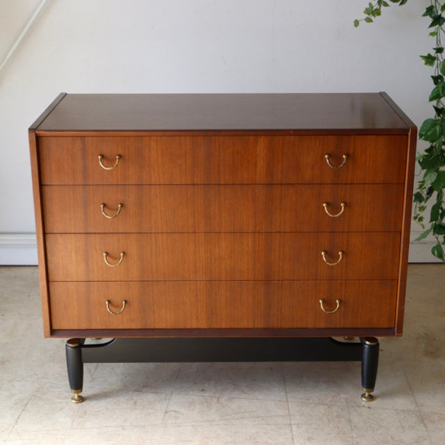 Vintage British mid-century G-Plan teak four-drawer chest with brass ring handles and tapered black legs with brass feet,.